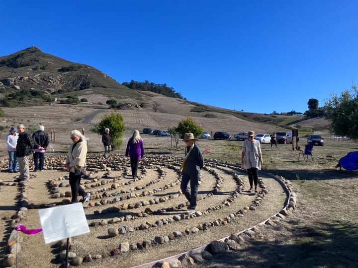 People walk thoughtfully through a circular path marked my stone border in a scenic location